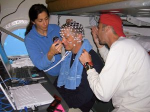 A NASA aquanaut is fitted with electrodes for an EEG experiment with assistance from two colleagues.