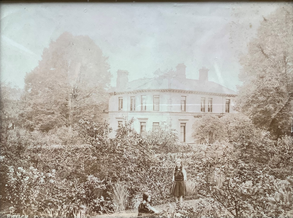 Lennoxvale, the house in Belfast which was the home of the Loewenthal family. Two small girls (Joan and Peggy) are shown in front of a hedge, behind which sits a substantial house.