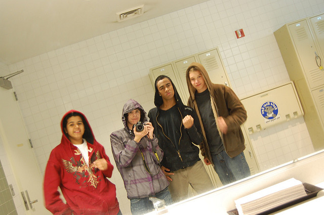 Four rough looking male students taking a picture with their hoodies on in the bathroom mirror