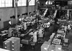 A photograph shows a warehouse full of people working with machines along assembly lines.