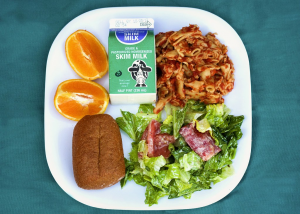 Healthier school lunch containing an orange, green salad, skim milk, and pasta with tomato sauce and a whole grain roll