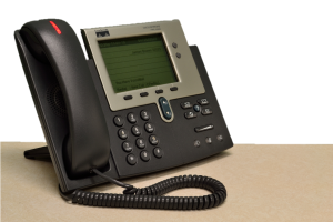 A black landline office phone sits on a tan table.
