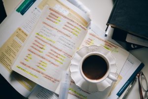 A cup of coffee sits on a notebook with notes of a world language scribbled down.