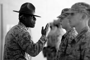 A group of soldiers stand at attention in front of a drill sergeant.
