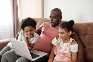 A father and his two young children watch a show on his laptop computer.