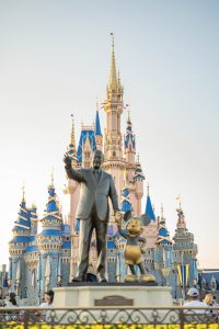 The statue of Walt Disney holding hands with Mickey Mouse in front of the castle at Walt Disney World.