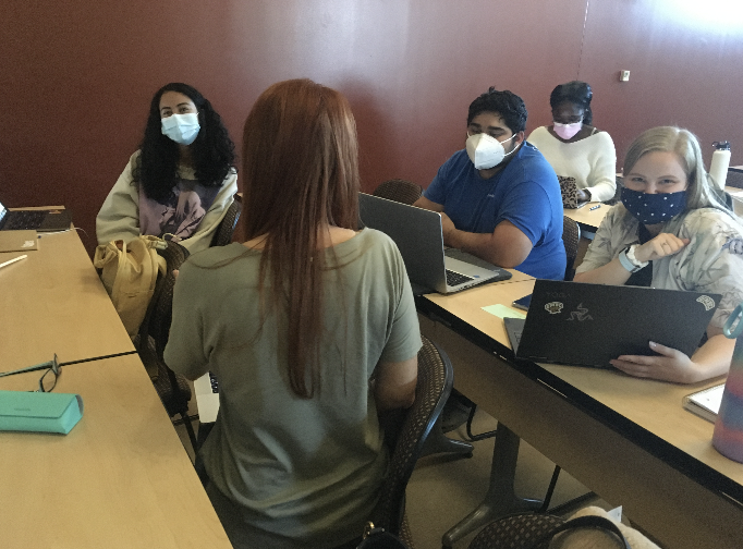 Students sitting face to face, wearing masks, in a classroom.
