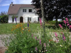 white farmhouse with trees and flowers around it