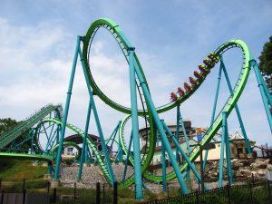 A green roller coaster with riders on a train car going around a curve.