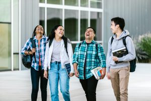 Four students laughing as they walk outside a building.