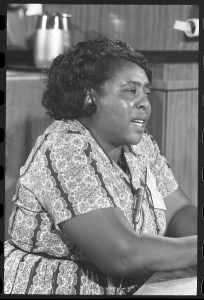 Black and white photo. Half-length portrait of Fannie Lou Hamer seated at a table.