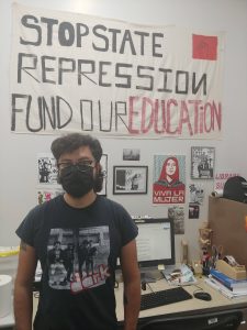 Johnny Rodriguez standing in front of a sign that says Stop State Repression Fund Our Education.