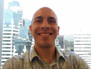 Octavio Hernandez smiling in front of a window overlooking high-rise buildings.